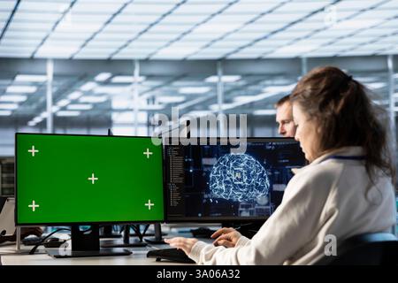 Woman in AI data center coding on green screen computers, upgrading equipment. IT engineers at PC desk overseeing artificial intelligence server clusters using mockup monitor Stock Photo