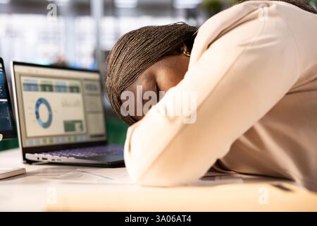 Exhausted businesswoman falling asleep at desk while monitoring and analyzing sales performance metrics and trends on laptop. Tired CEO dozing off while managing budgets on notebook Stock Photo