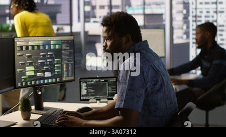 Computer scientist resuming work after strolling in workspace, doing software debugging using PC. Man walking with tablet in office, fixing coding issues using computer, camera A Stock Photo