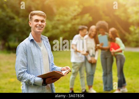 Student Guy Preparing For Exam Outdoor While His Friends Chatting On Background Stock Photo
