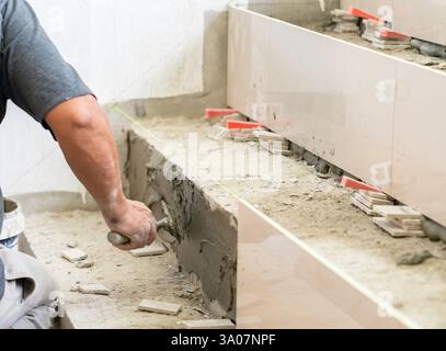 Worker  tiling stairs, applying adhesive on step. Process of installation of tiles. Stock Photo
