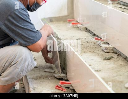 Worker laying ceramic tiles on stairs. Tiler, New apartment. Stock Photo