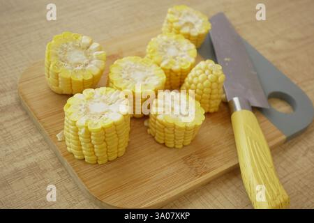 Freshly cut corn cobs on a wooden cutting board with a knife Stock Photo