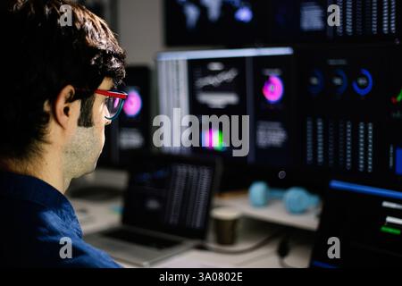 Stock trader analyzing charts on multiple computer screens in office at night Stock Photo