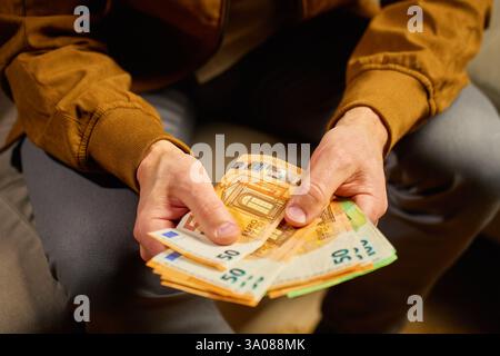 Close-up of man counting euro banknotes at home. Person planning his personal finances, sitting on sofa with cash money. Concept of planning home budget, savings and personal finances Stock Photo