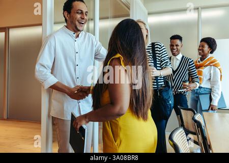 A group of colleagues sharing a joyful and positive moment in an office setting. The image captures a friendly greeting with handshakes, showcasing te Stock Photo