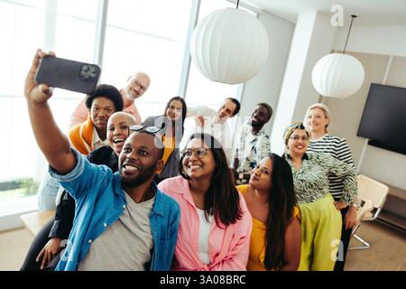 A joyful group gathers for a selfie in a modern office, showcasing diversity and teamwork. The casual atmosphere emphasizes camaraderie and positive c Stock Photo