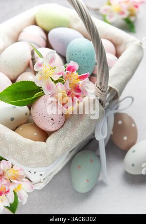 Colorful easter eggs and spring flowers overflowing from a white wicker basket on a light background Stock Photo