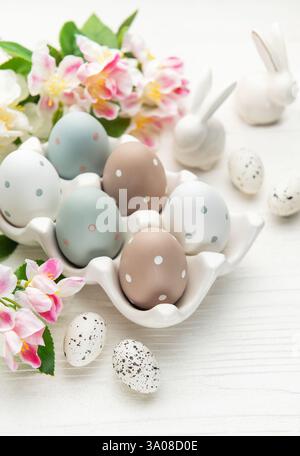 Easter eggs with spring flowers and ceramic bunnies are celebrating easter sunday on a white wooden table Stock Photo