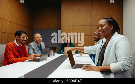 A group of corporate professionals sit around a sleek conference table, engaged in a lively meeting. The setting reflects a modern environment with di Stock Photo