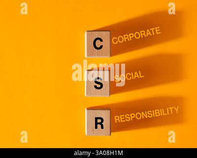 Wooden blocks with acronym CSR, standing for corporate social responsibility on yellow background. Stock Photo