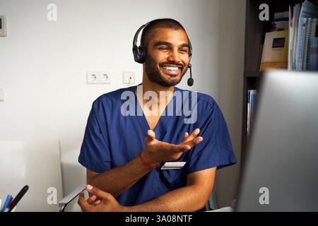 Happy male medical professional wearing headset assisting patient through video call in clinic at hospital Stock Photo