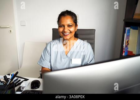 High angle portrait of smiling female doctor wearing scrubs sitting on chair in clinic Stock Photo
