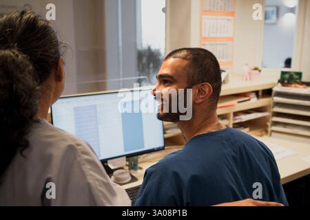 Smiling male doctor talking with female coworker while working on desktop PC in hospital Stock Photo
