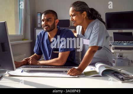 Smiling female medical professional standing near male coworker using desktop PC while working in hospital Stock Photo