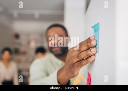 Hand of male entrepreneur sticking adhesive note on whiteboard in meeting room at office Stock Photo