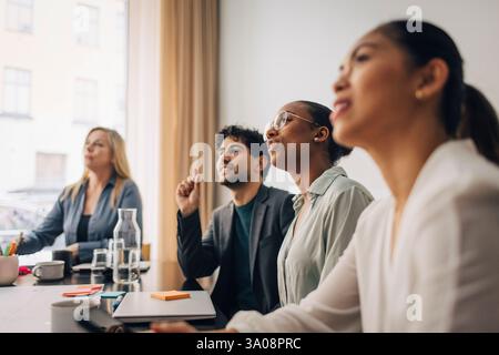 Young businesswoman wearing eyeglasses sitting with male and female coworkers in meeting room at office Stock Photo