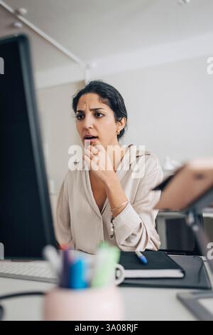 Confused female creative professional using desktop PC while sitting at desk in office Stock Photo