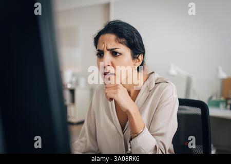 Confused female creative professional using desktop PC while sitting with hand on chin in office Stock Photo