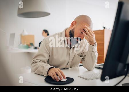 Stressed businessman sitting with head in hand at office desk Stock Photo