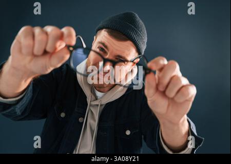 Funny guy playing with glasses. Handsome man is in the studio against blue background. Stock Photo