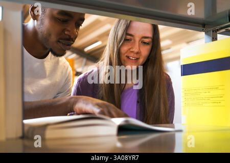 Multiracial male and female students reading book in bookshelf at university library Stock Photo