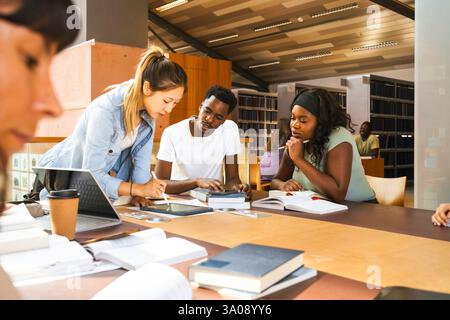 Multiracial friends discussing assignment over digital tablet at desk in university library Stock Photo