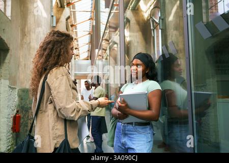 Young female friends talking while standing in college corridor Stock Photo