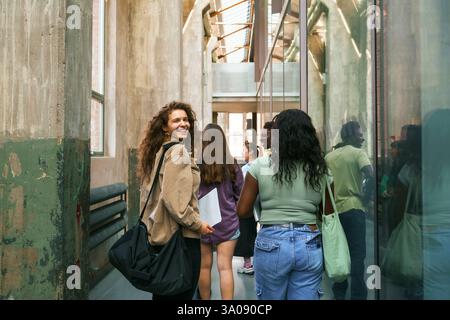 Portrait of cheerful young female student walking with friend in corridor at college Stock Photo