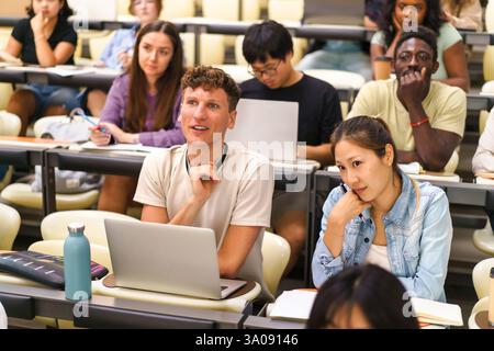 Multiracial male and female students sitting at desks in university lecture hall Stock Photo