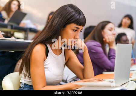 Young female student using laptop while sitting in lecture hall at university Stock Photo