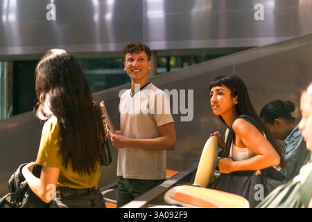 Smiling male student standing near female friends in classroom at college Stock Photo
