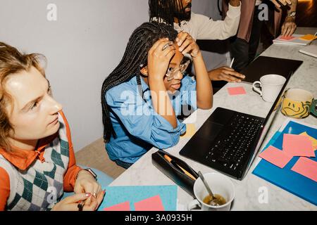High angle view of female entrepreneur with head in hand sitting in meeting amidst colleagues at office Stock Photo