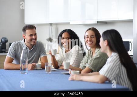 Interracial friends drinking and talking in the kitchen at home Stock Photo
