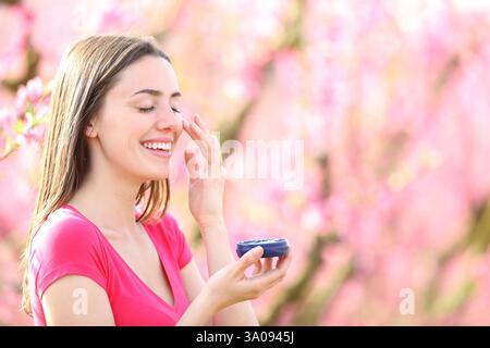 Happy candid woman applying hydration cream on cheek in a field in spring Stock Photo