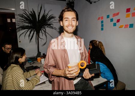 Portrait of smiling male business professional holding digital tablet and mug at office Stock Photo