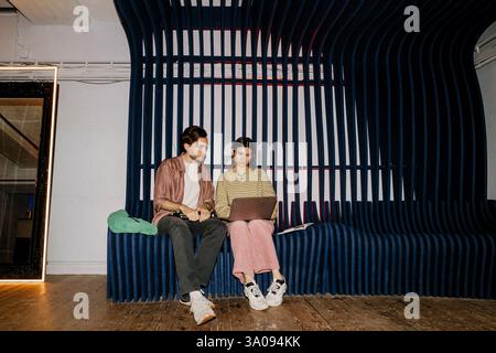 Male and female business professionals using laptop while sitting on seat at office Stock Photo