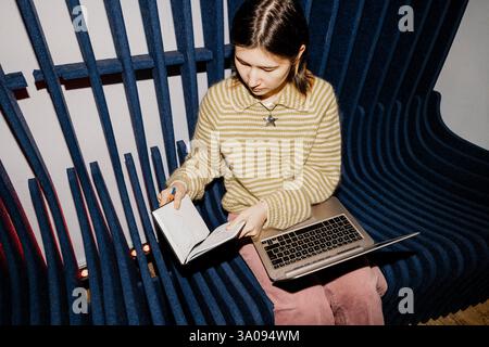 High angle view of female entrepreneur reading diary while sitting on seat with laptop at office Stock Photo