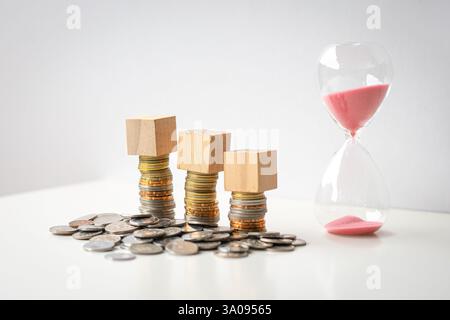 3 blank wooden square blocks on top of coins, next to sand timer. Isolated on white background. Stock Photo