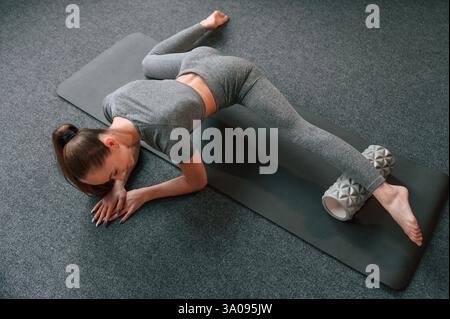 In yoga clothes. Doing stretching. Young woman doing fitness indoors. Stock Photo