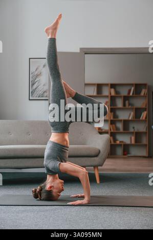Making headstand. Young woman in yoga clothes doing fitness indoors. Stock Photo