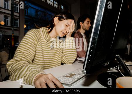 Sad female computer programmer with head in hand sitting at desk Stock Photo