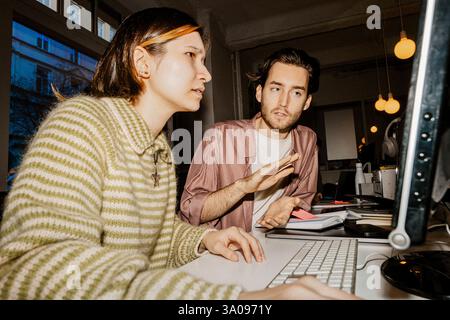 Male entrepreneur assisting female colleague working on computer at office Stock Photo