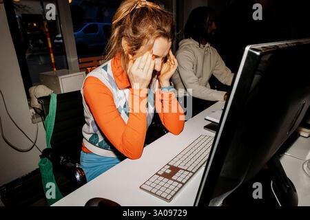 Frustrated female entrepreneur touching temples while sitting at desk in office Stock Photo