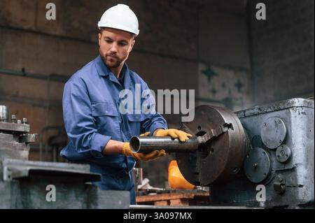 Operating the automatic machine. Factory worker in blue uniform is indoors. Stock Photo