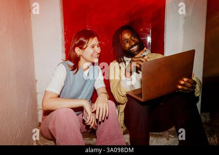Happy male entrepreneur pointing while sitting with laptop next to female colleague Stock Photo