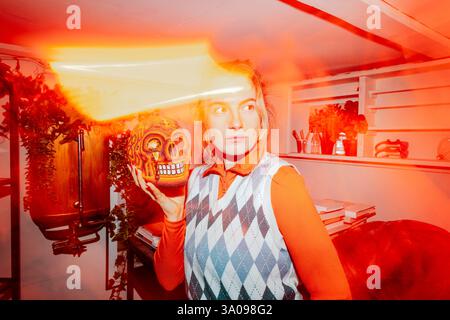 Businesswoman holding artificial human skull and looking away amidst bright orange lights Stock Photo