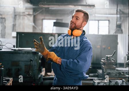 Working by using digital tablet. Man at the factory that is in blue uniform is indoors. Stock Photo