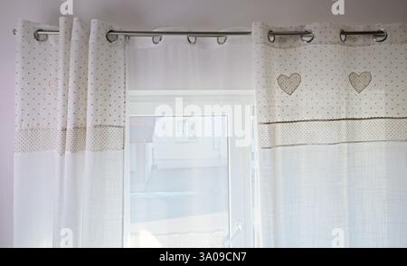 Vintage white curtains on metal rings on natural material with embroidered hearts at home. Cleaning and cleanliness. Interior and textiles.  Stock Photo