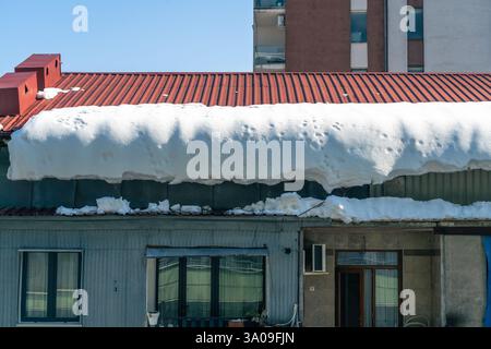 Heavy snow weighing down on a residential roof with large icicles and melting ice creating a hazardous winter scene. Stock Photo